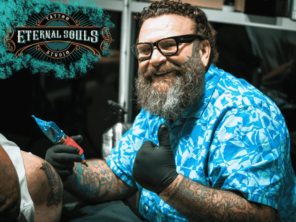 Tattoo artist Eric Coe smiling while working on a custom leg tattoo inside Eternal Souls Tattoo Studio in Corinth, Texas